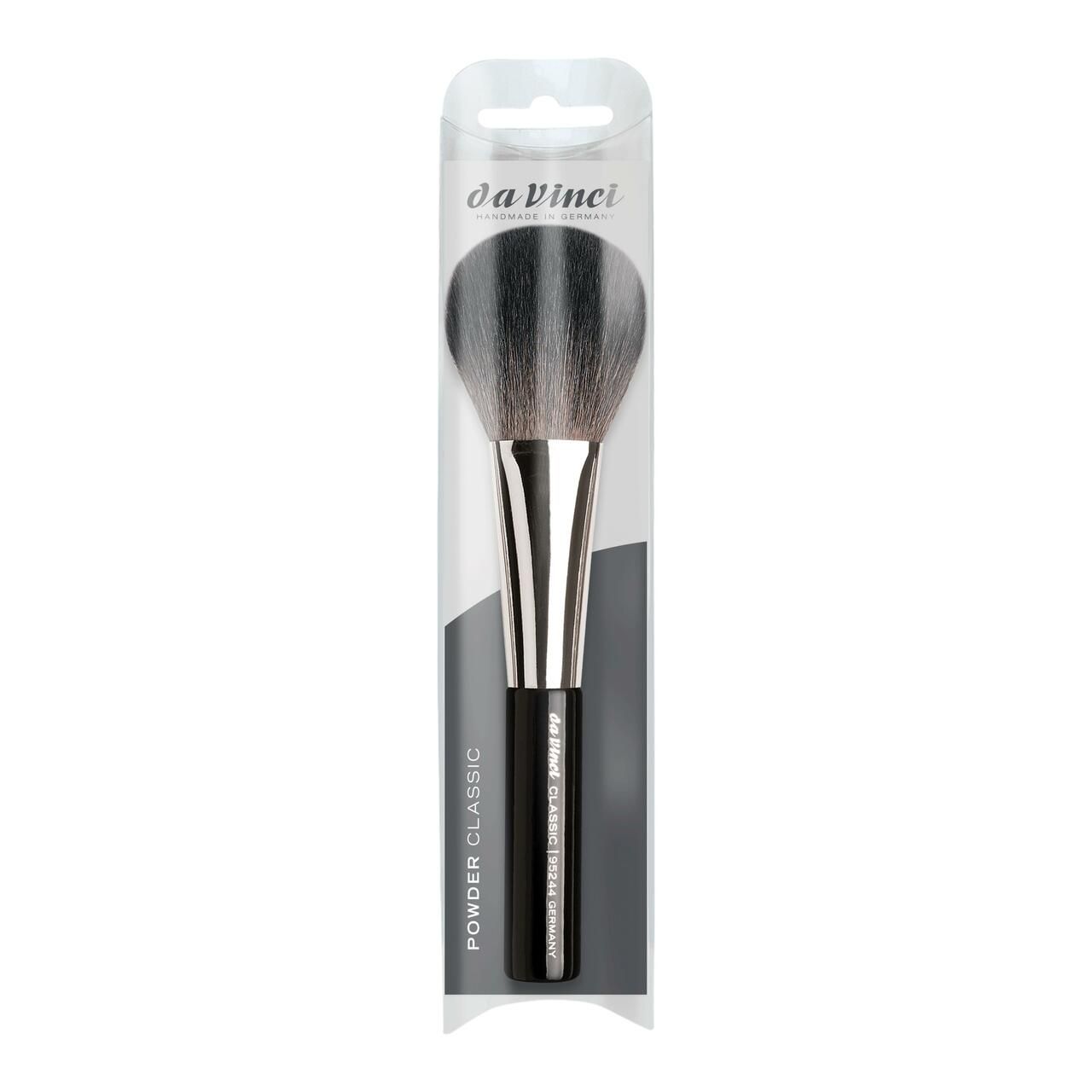 Puderpinsel in Verpackung. Schwarzer Pinselkopf, silberfarbene Metallhülse, schwarzer Griff. Aufschrift.