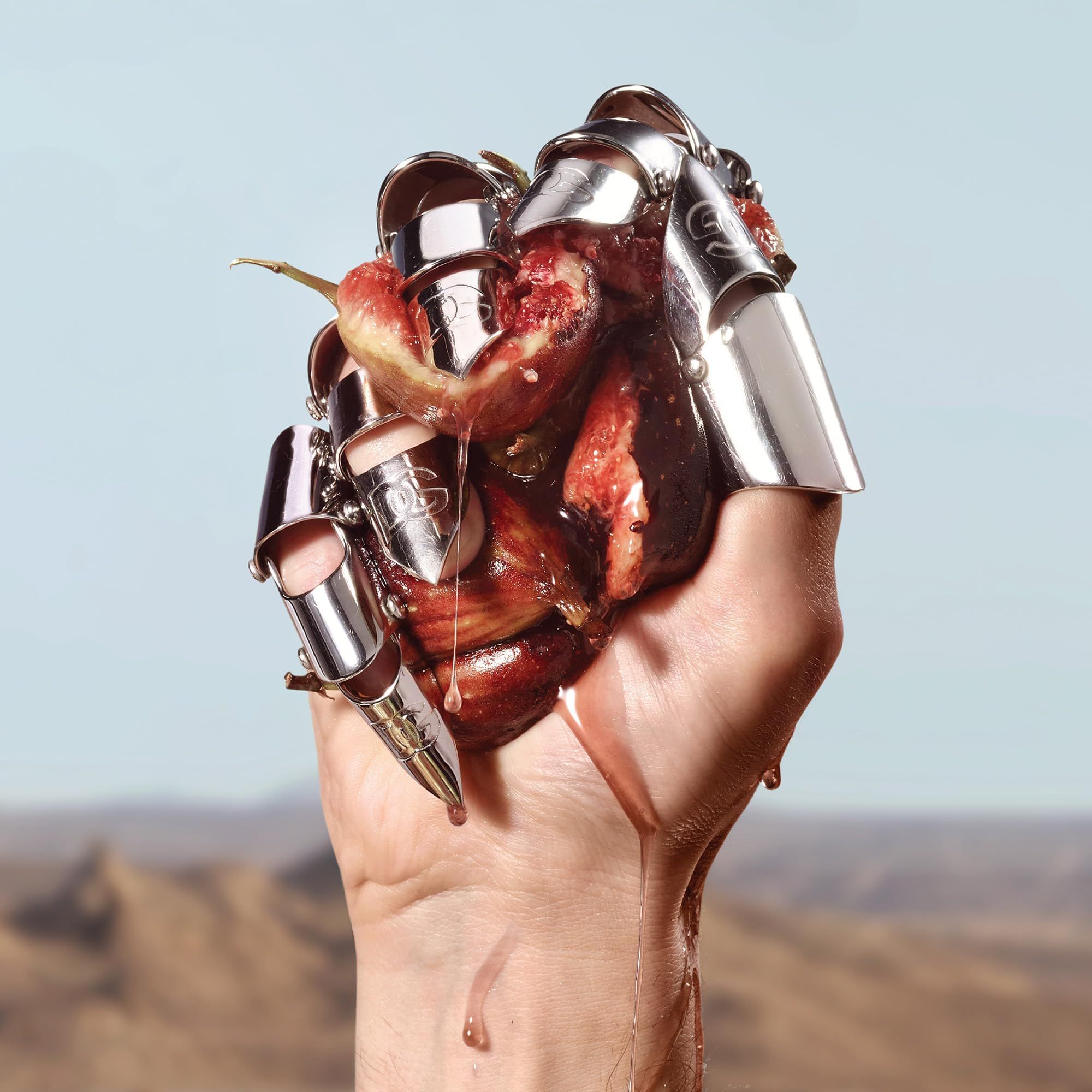 Hand mit silbernen Ringen hält Feigen. Saft tropft. Wüstenhintergrund.