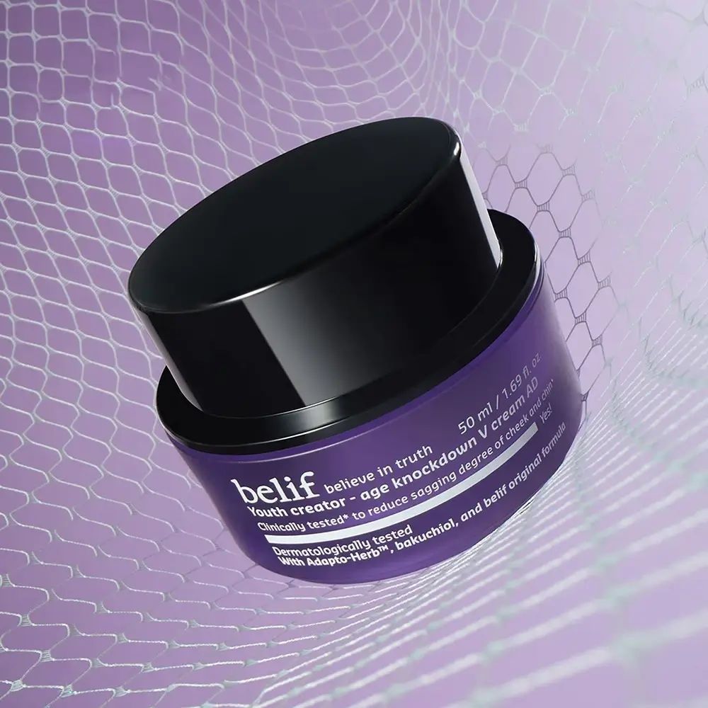 Lila Tiegel mit schwarzem Deckel, leicht geöffnet. Aufschrift: belif, Youth creator - age knockdown V cream AD. Text: Klinisch getestet, mit Adapt-Herb.
