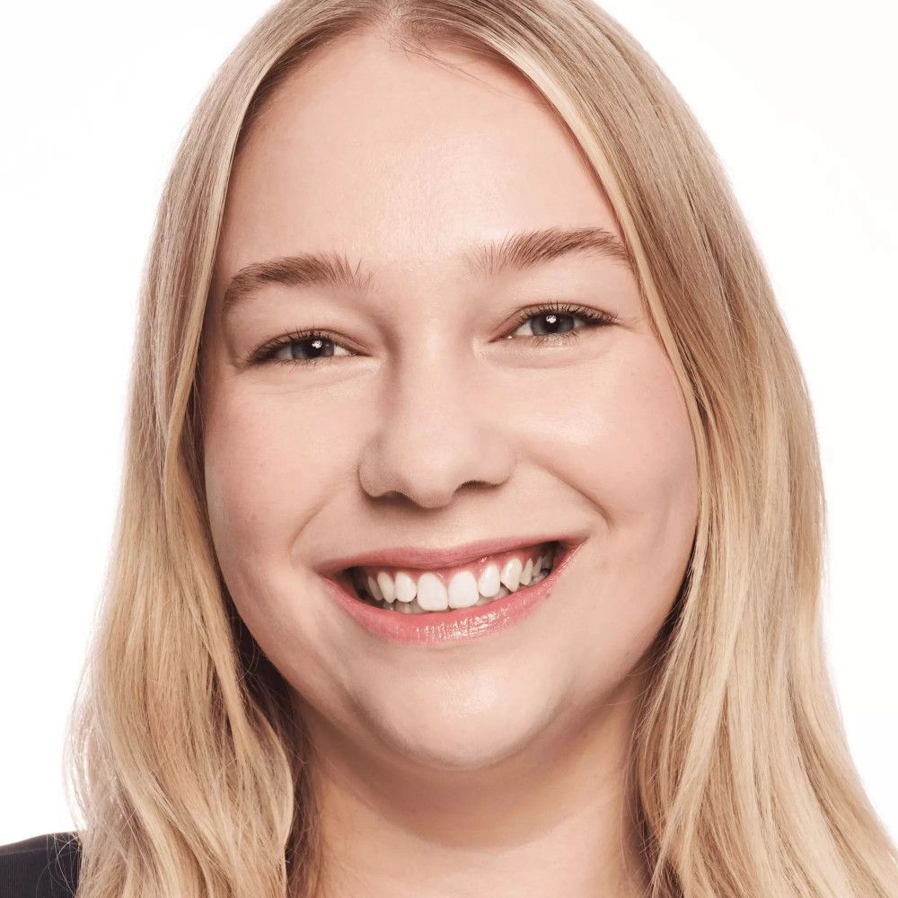 Porträt einer Frau mit blonden Haaren. Sie lächelt. Ebenmäßiger Teint.