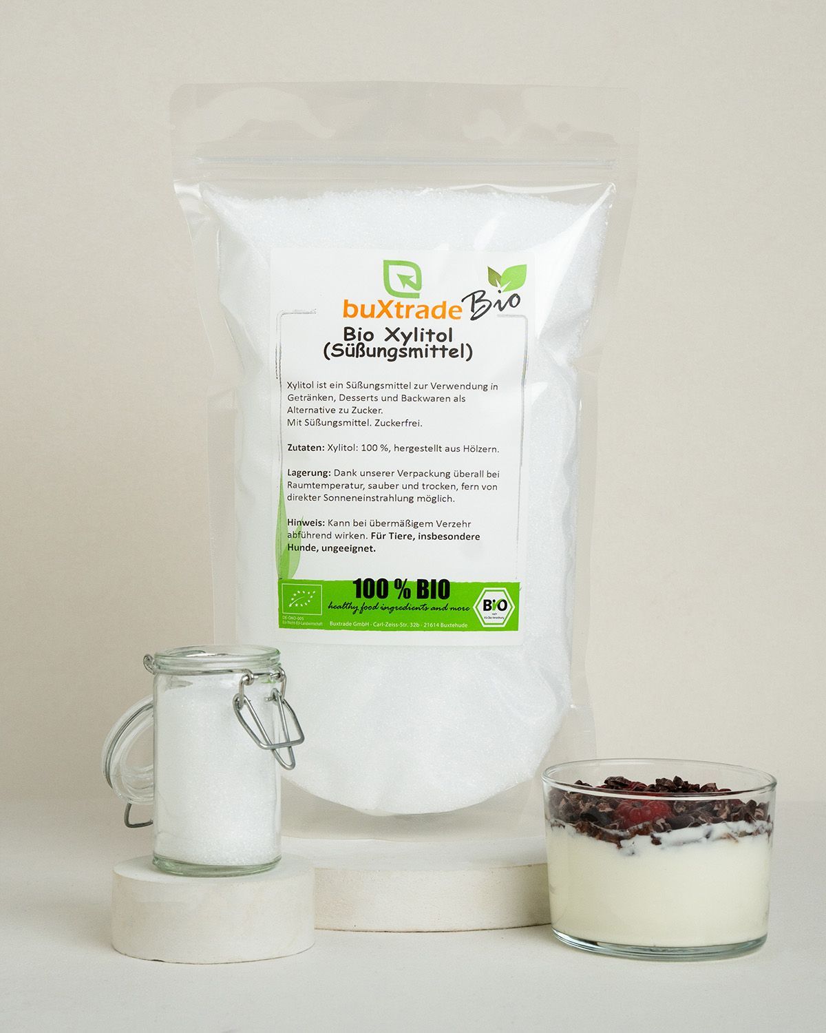 Buxtrade Bio Xylitol Süßungsmittel in einem Standbeutel, daneben ein Glas mit Xylitol und ein Dessert.