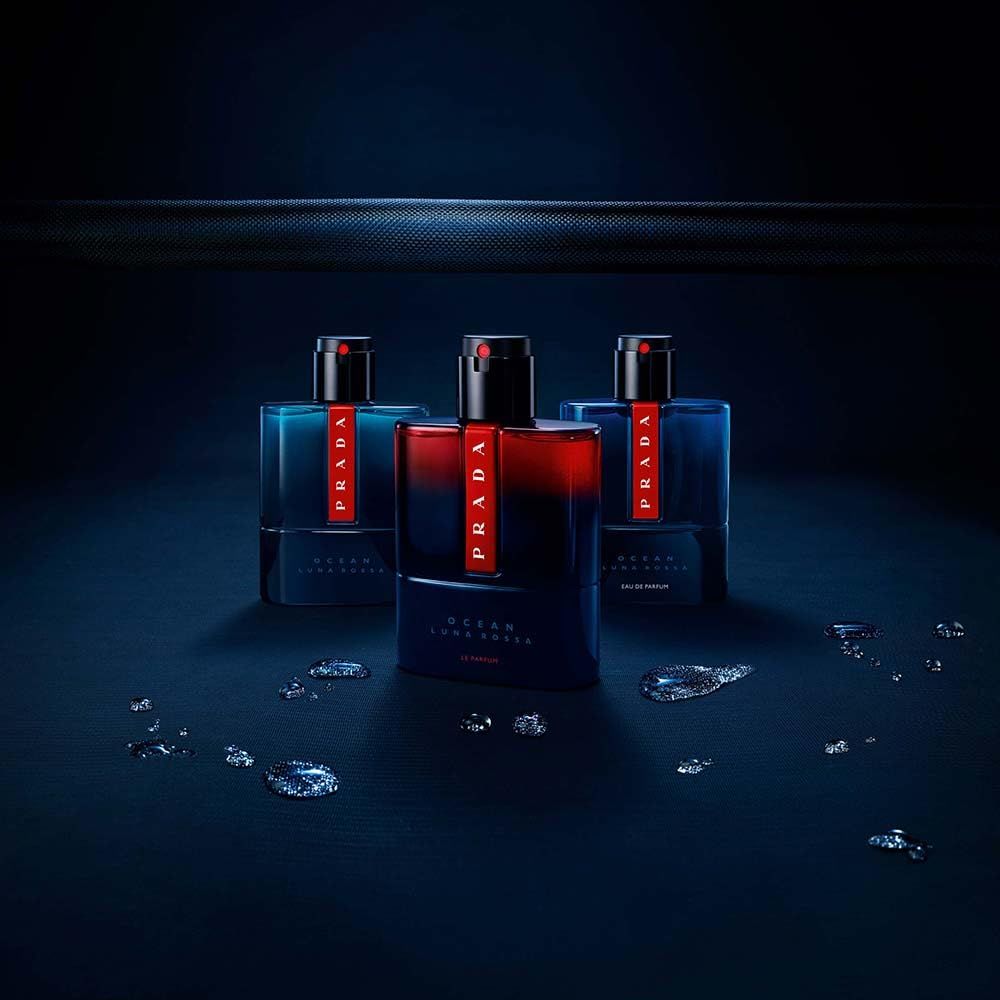 Drei Flakons Prada Luna Rossa Ocean Le Parfum. Blaue Glasflaschen mit rotem Prada-Logo. Tropfen auf dunklem Hintergrund.