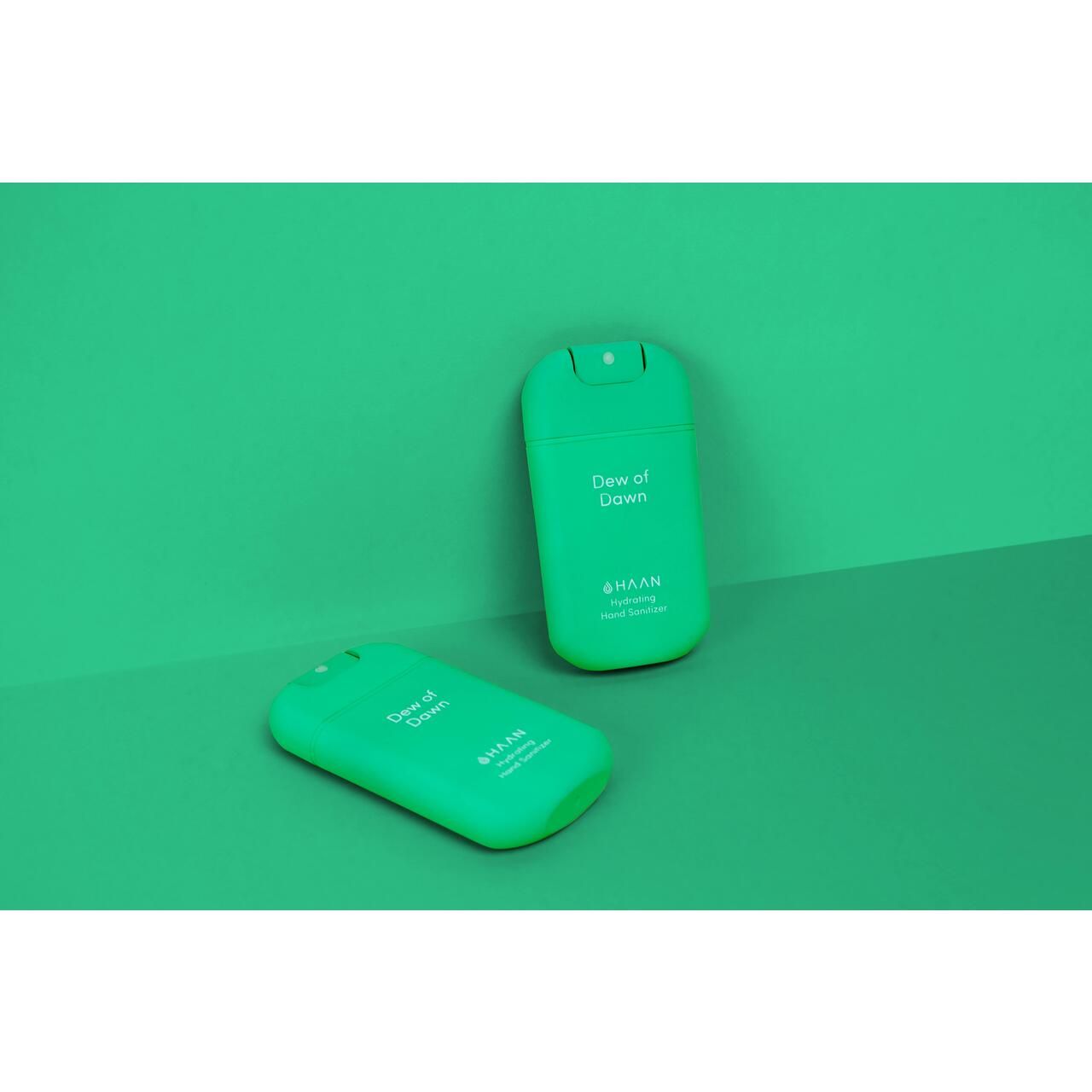 Zwei grüne Handdesinfektionsmittel-Taschenzerstäuber. Auf einem steht "Dew of Dawn", darunter "HAAN Hydrating Hand Sanitizer".