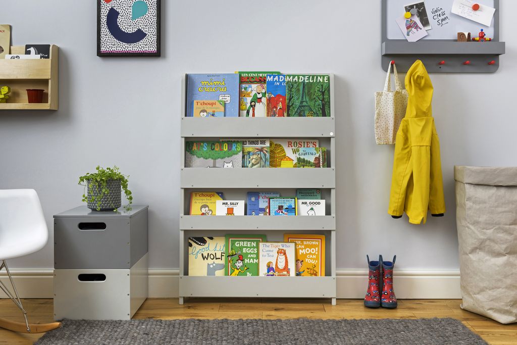 Hellgraues Bücherregal mit Büchern in einem Raum. Bücher mit farbigen Einbänden. Der Raum hat eine graue Wand, einen Teppich und einen Stuhl.