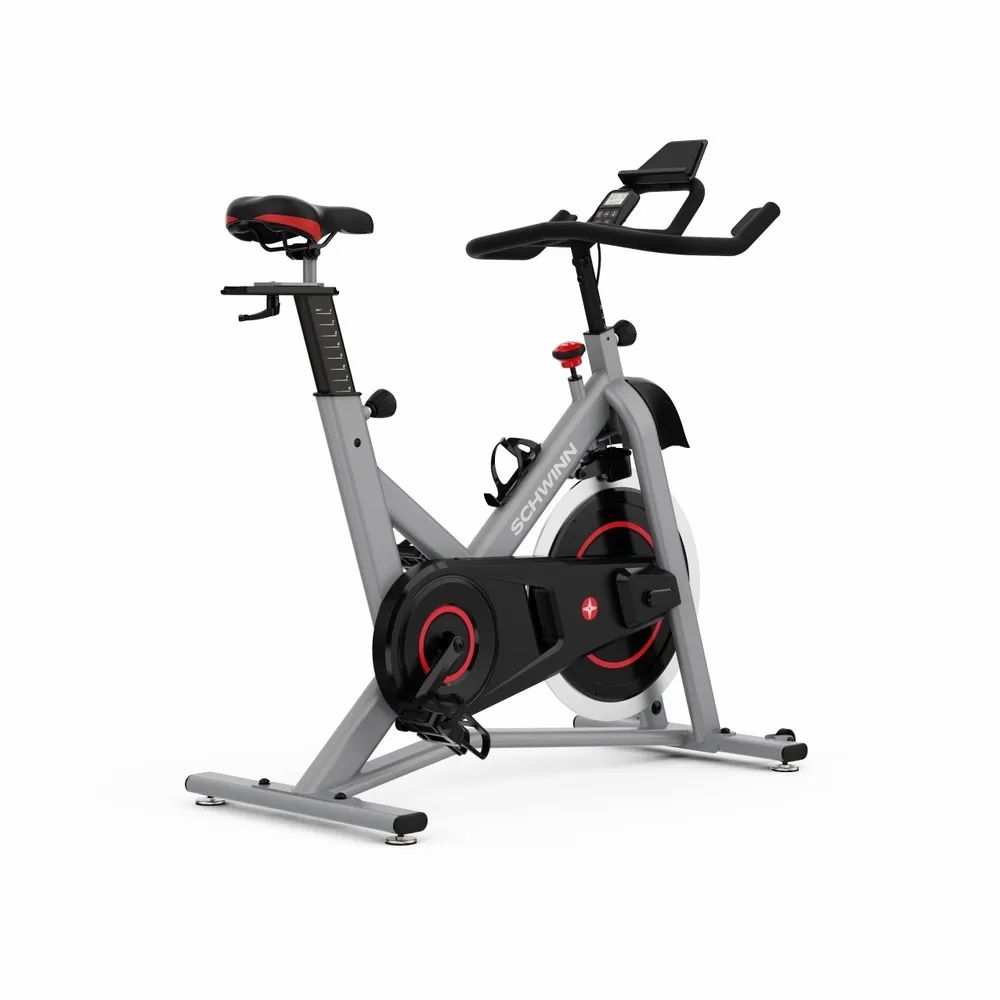 Grauer Heimtrainer mit rotem Akzent. Schwarzes Schwungrad, Lenker, Sattel und Pedale. Marke: Schwinn. Wasserflaschenhalterung.