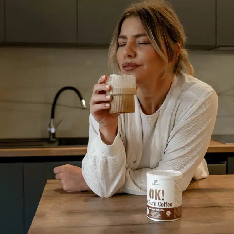 Frau trinkt Kaffee neben einer Dose OK! FatBurn Coffee am Küchentisch.