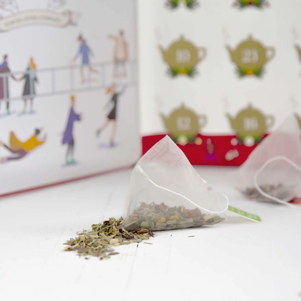 Teebeutel mit losem Tee daneben. Adventskalender im Hintergrund mit Teekannen-Motiven und Zahlen.