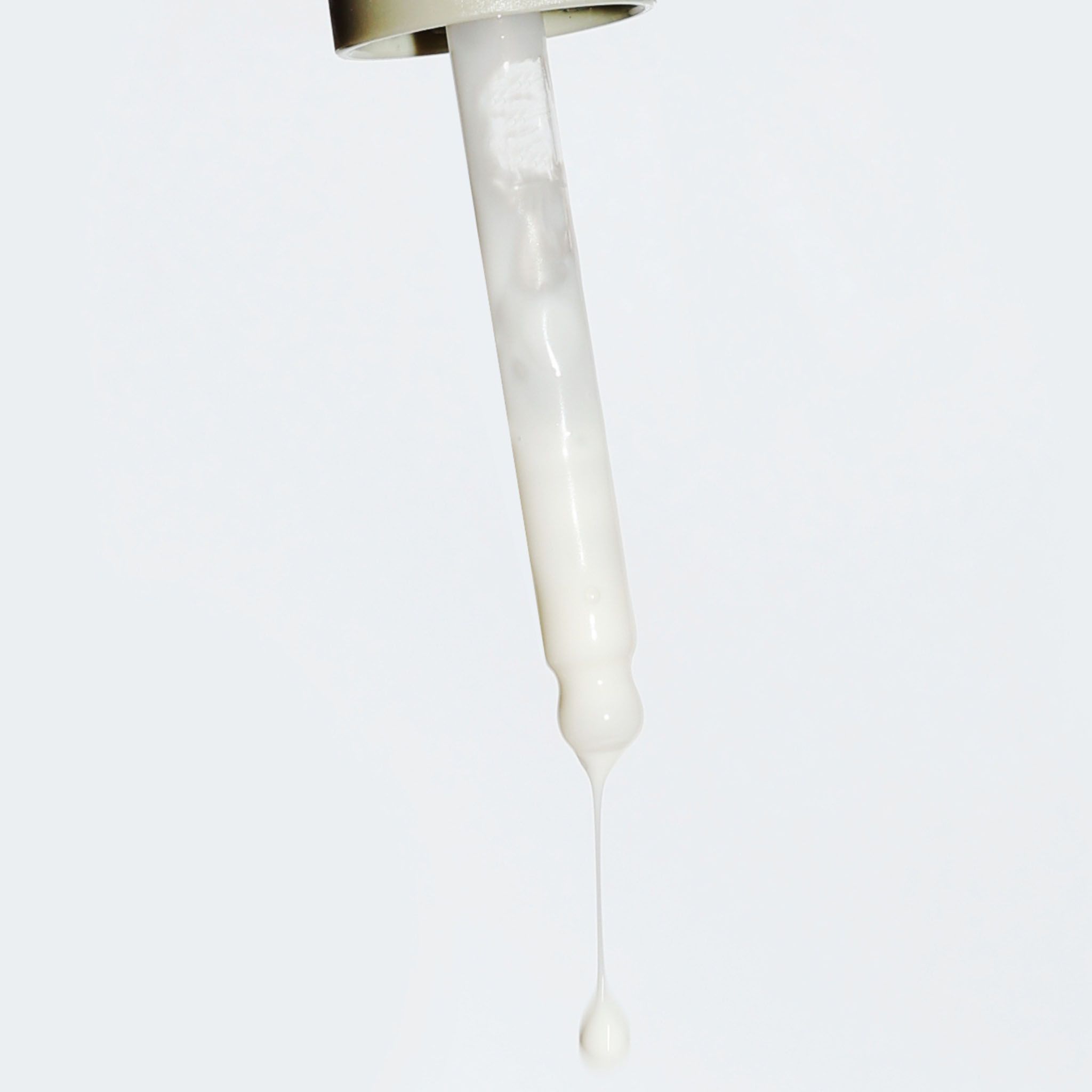 Pipette mit einem Tropfen eines weißen Serums, das von der Spitze hängt.