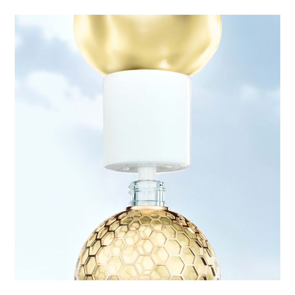 Flakon mit goldfarbenem Deckel und weißem Verschluss. Glasflakon mit gelber Flüssigkeit. Blauer Hintergrund.