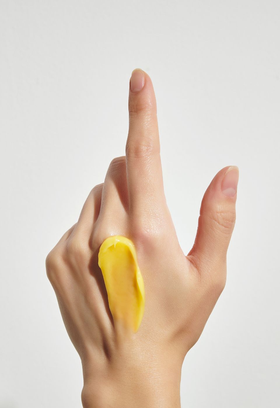 Hand mit gelber Creme auf der Haut. Hintergrund weiß.