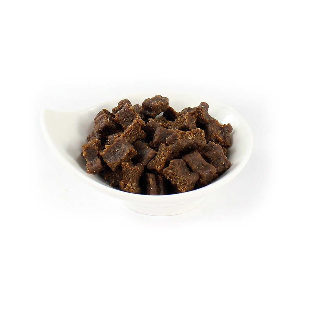 Braune, quadratische Hundesnacks in einer weißen, geschwungenen Schale. Die Snacks sind grob strukturiert.