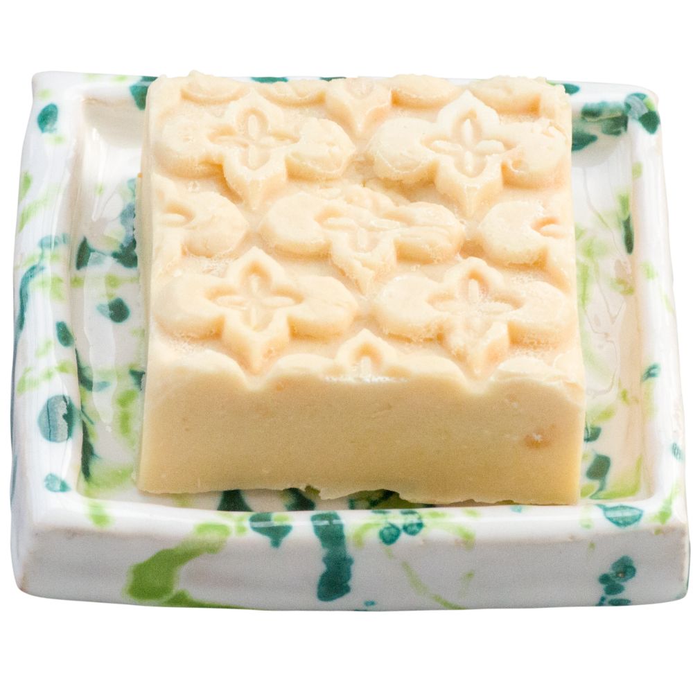 Rechteckige Seife mit floralem Muster auf einer Seifenschale mit grün-weißer Marmorierung.