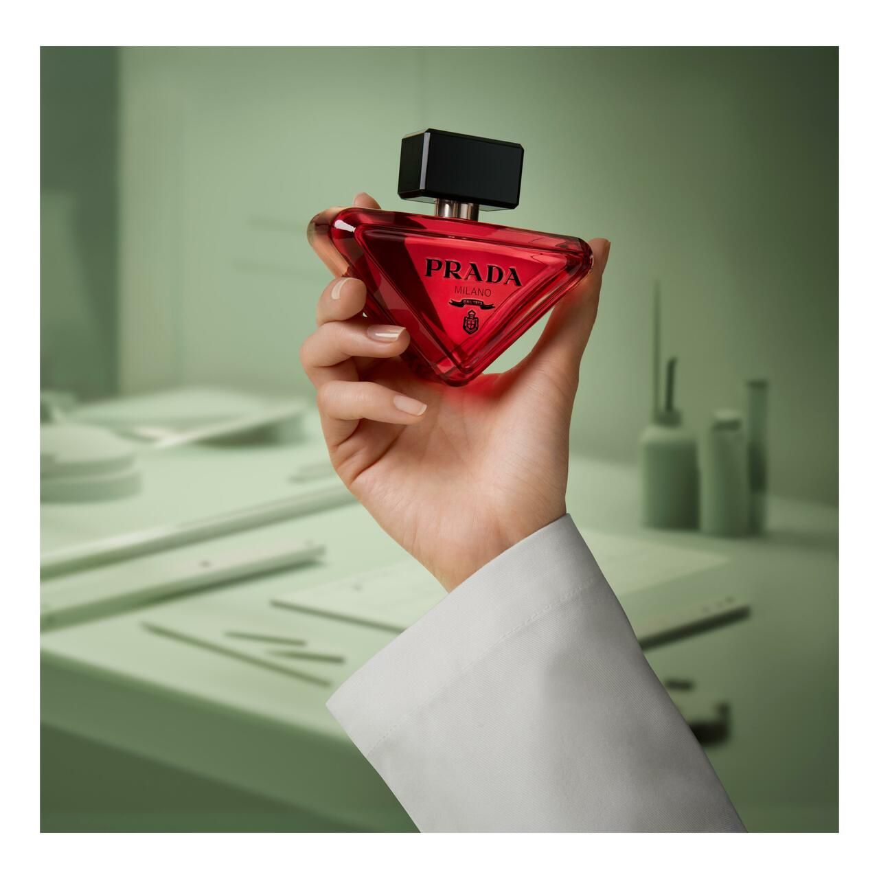 Roter Flakon in einer Hand. Schwarzer Deckel. Prada-Logo. Hintergrund mit Laborutensilien.