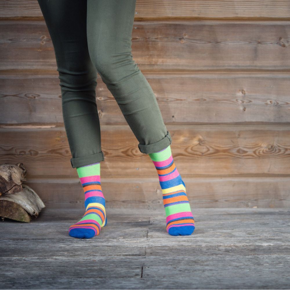 Person trägt bunte Kniestrümpfe mit horizontalen Streifen. Farben: Blau, Grün, Orange, Gelb und Pink. Marke: SupCare.