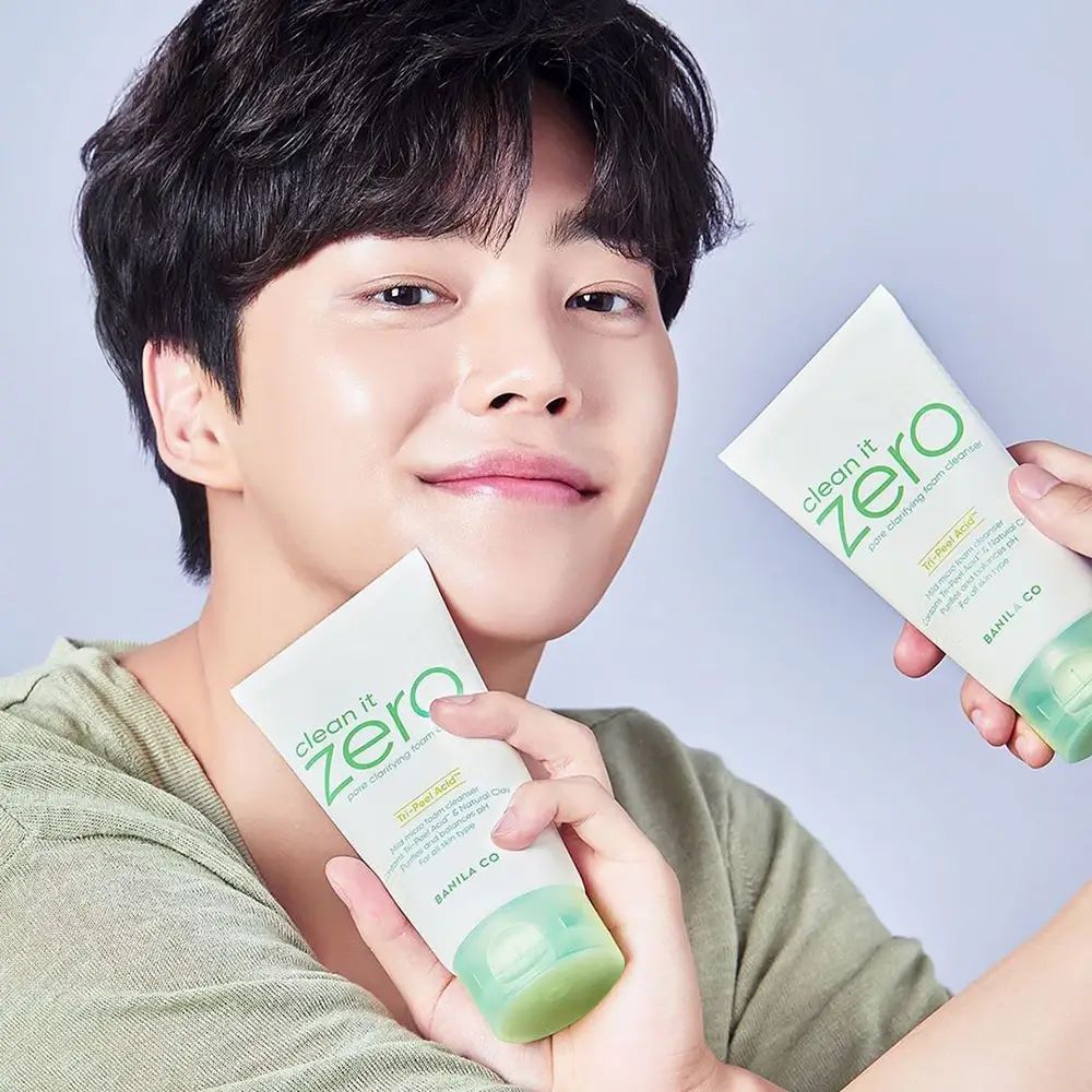 Mann hält zwei Tuben. Aufschrift: Clean It Zero, Pore Clarifying Foam Cleanser. Text: Tri-Peel Acid, BANILA CO. Grüner Hintergrund.