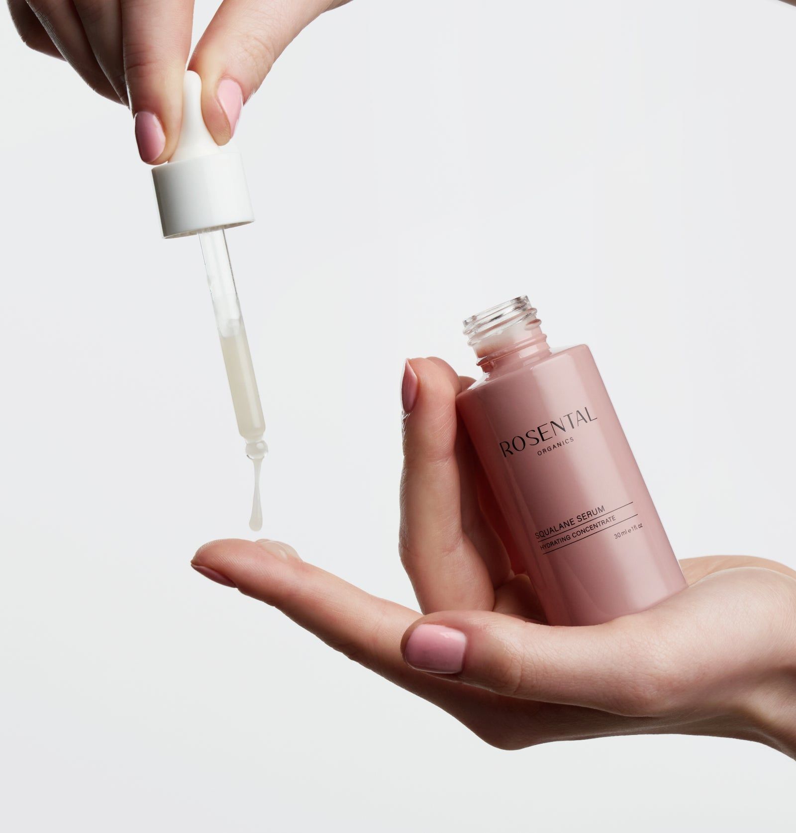 Hände halten eine Flasche und eine Pipette. Serum tropft aus der Pipette auf die Handfläche. Rosa Flasche mit Etikett.