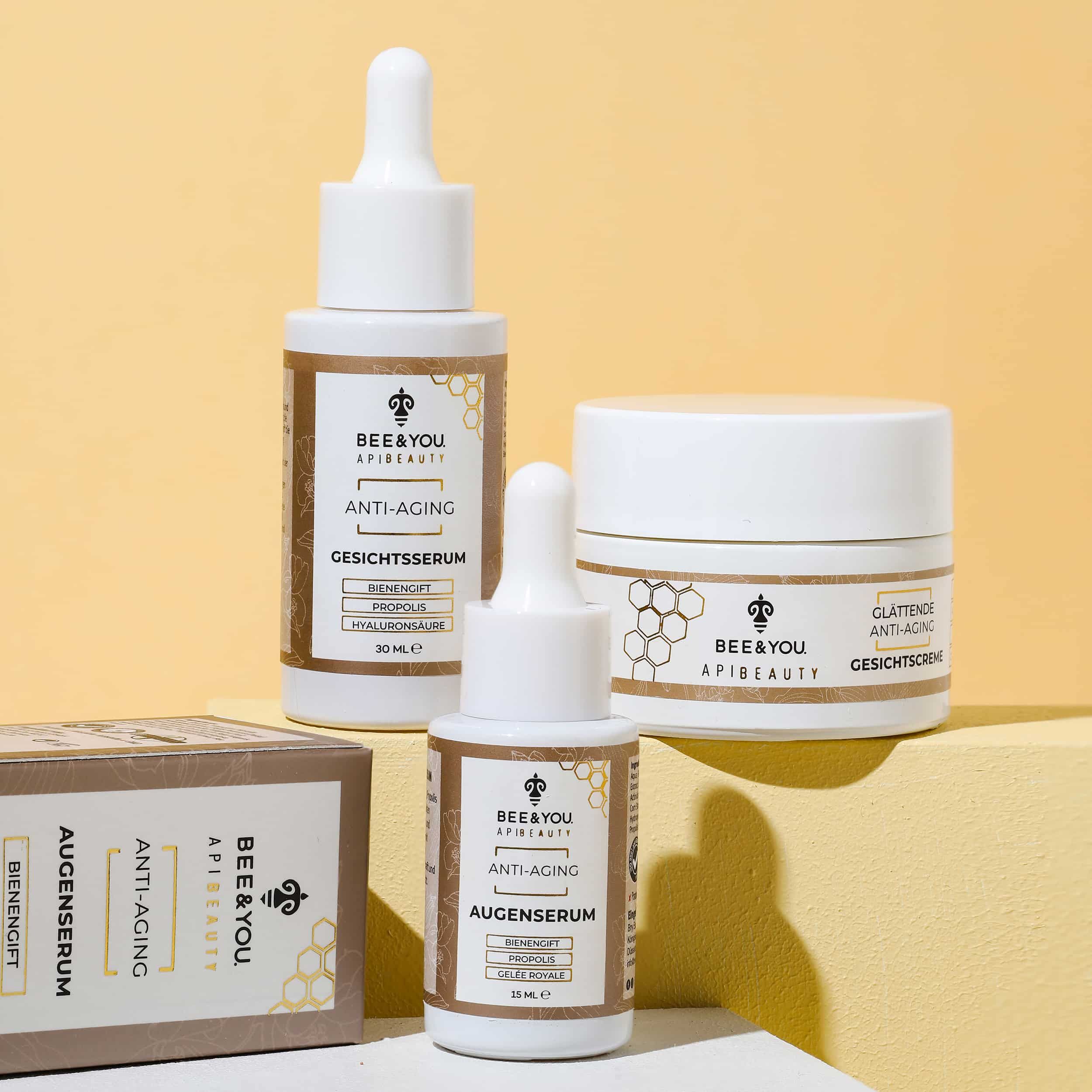 Drei Produkte: Augenserum, Gesichtscreme und Gesichtsserum. Weiße Tiegel und Flaschen mit braunen Etiketten.