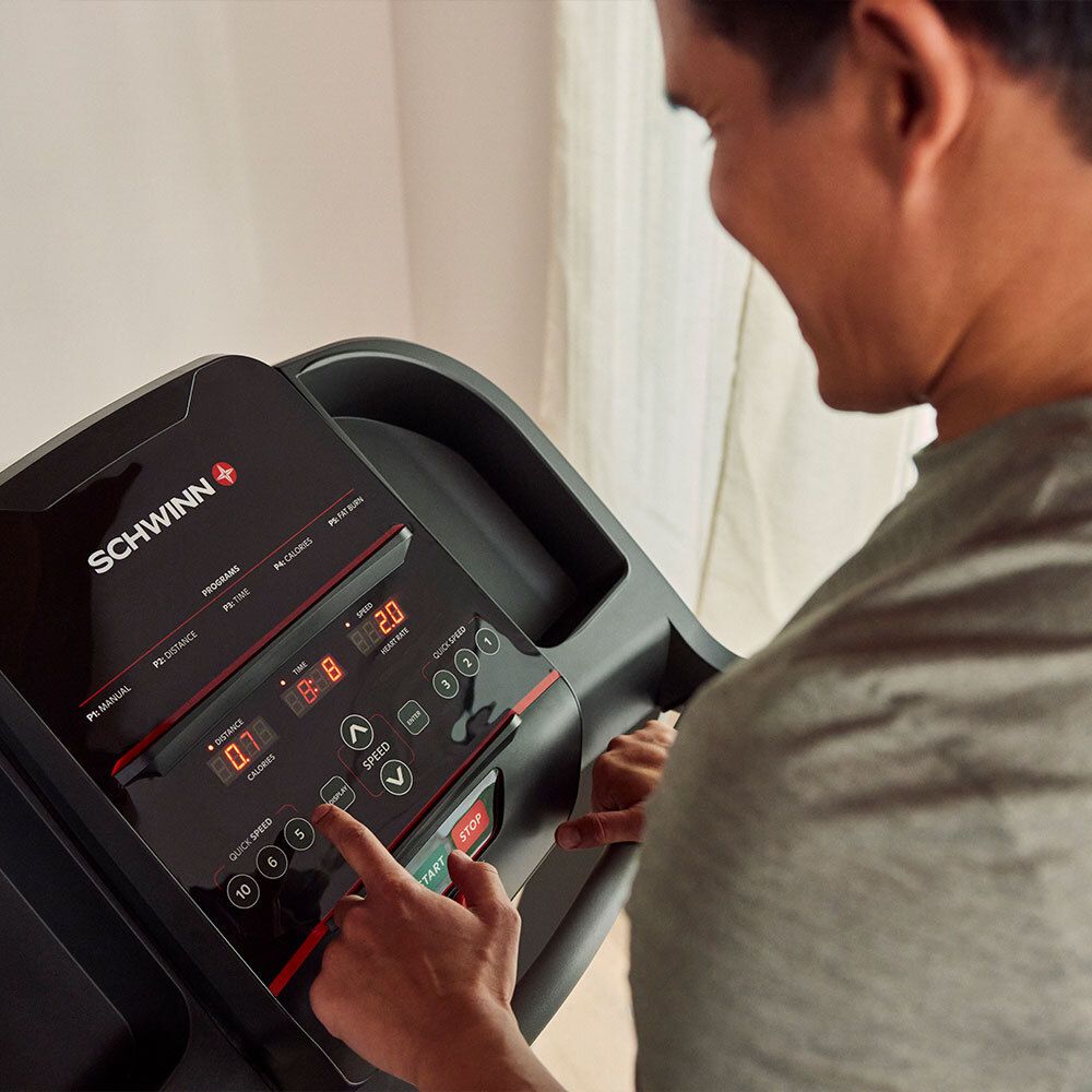 Person bedient die Konsole eines Laufbands. Schwarzes Bedienfeld mit Display und Tasten. Schwinn-Logo.