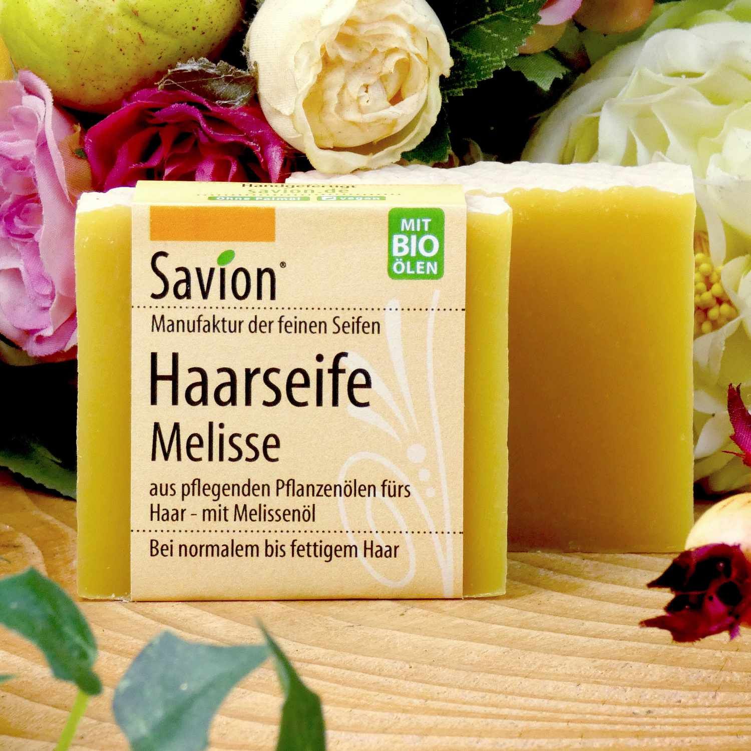 Zwei gelbe Seifenstücke mit Blumen. Das vordere hat ein Etikett mit Produktname und Marke. Aufschrift: Haarseife Melisse.