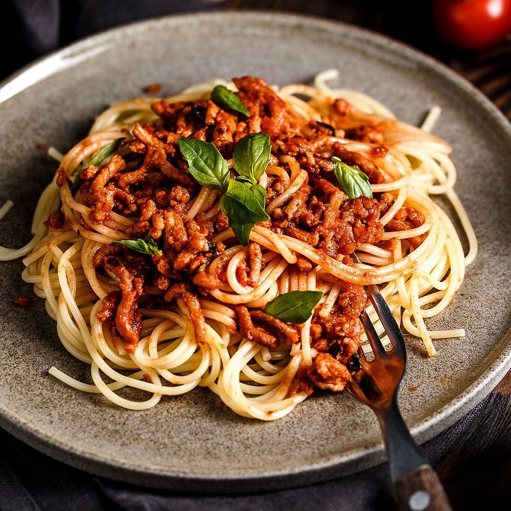 Teller mit Spaghetti Bolognese. Tomatensauce, Hackfleisch und Basilikumblätter. Gabel.