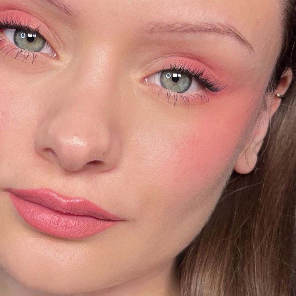 Nahaufnahme eines Gesichts mit rosa Make-up auf Augen, Wangen und Lippen. Grüne Augen.