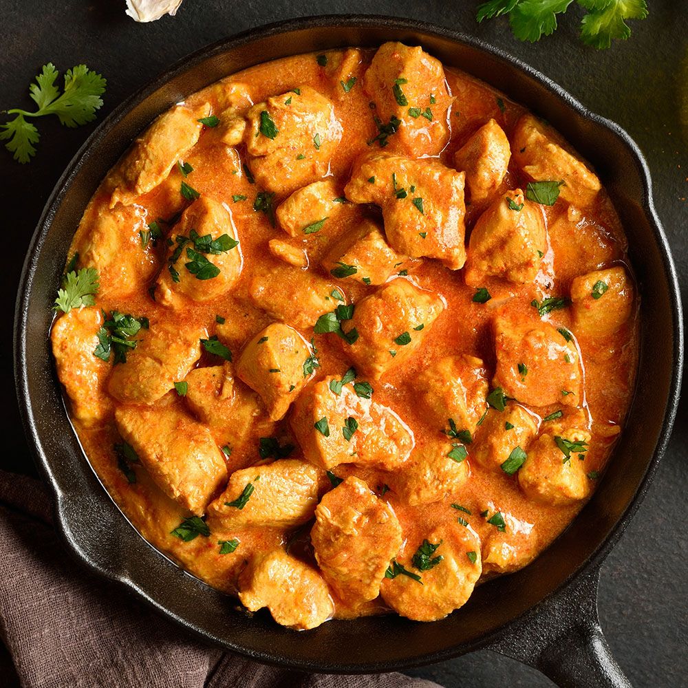 Hühnchen Tikka Masala in schwarzer Pfanne. Orangefarbene Soße, Hühnerstücke, Kräuter. Draufsicht.