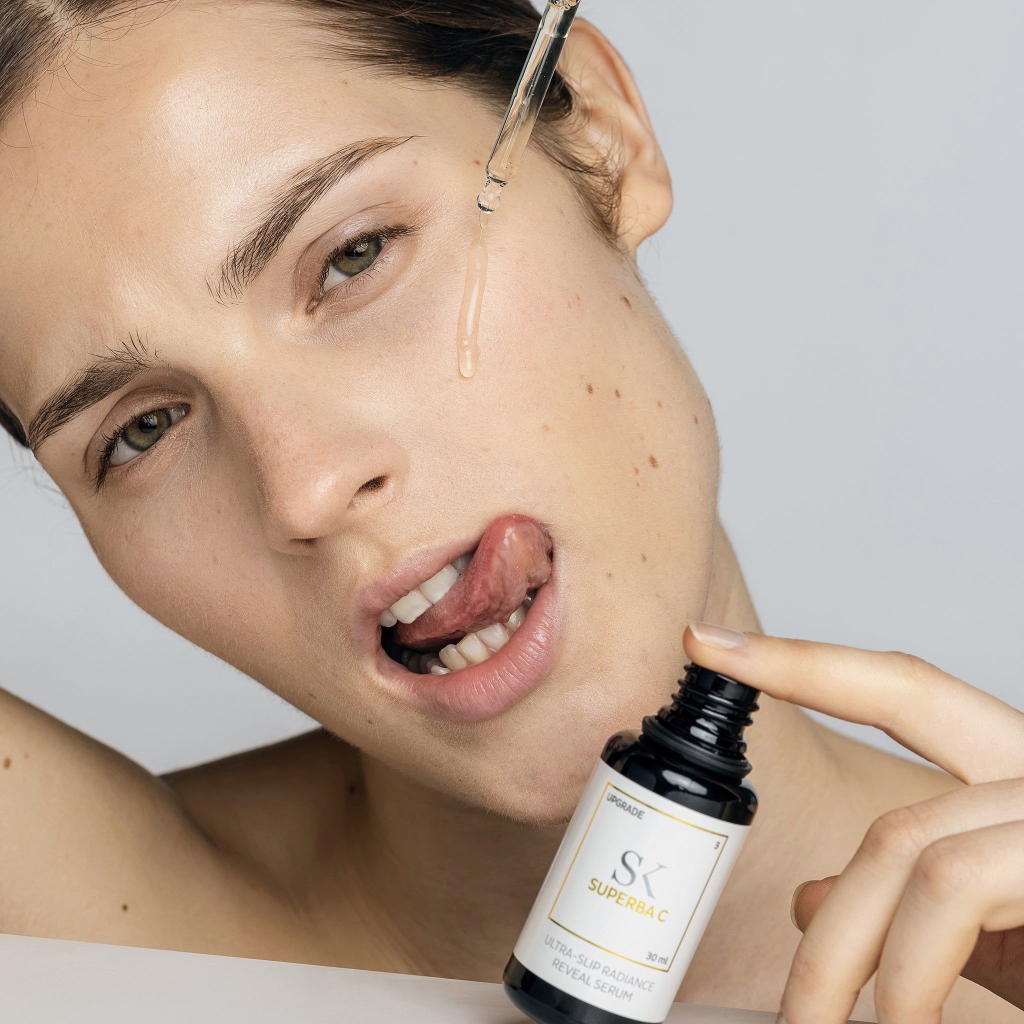 Frau mit Flasche und Pipette. Auf dem Etikett steht "SK Superba C" und "Ultra-Slip Radiance Reveal Serum".