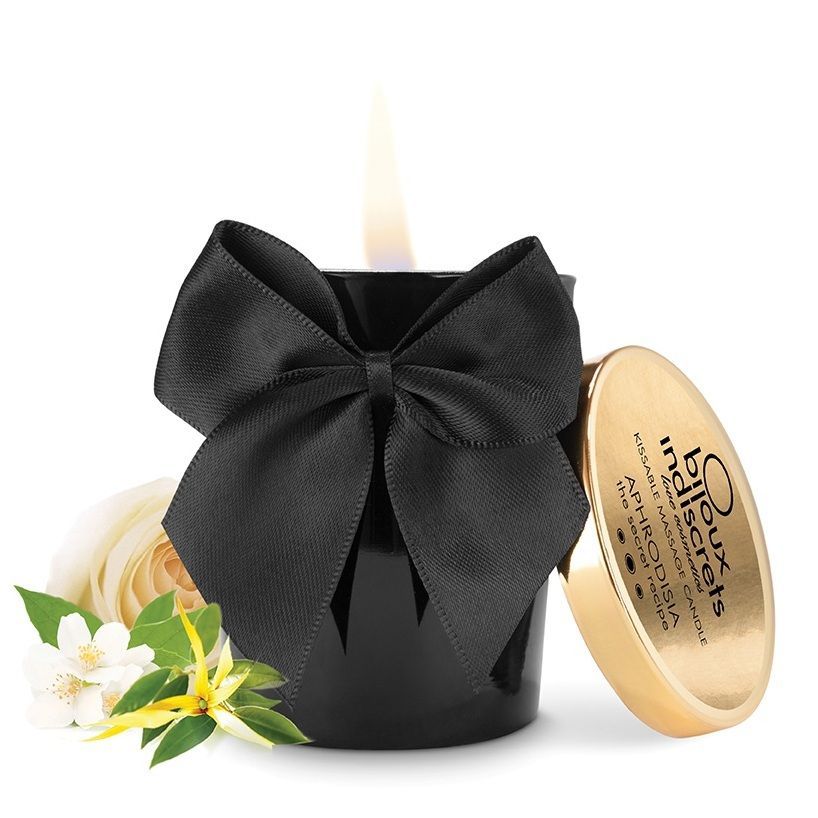 Schwarze Kerze mit Schleife, Deckel und Blumen. Goldener Deckel mit Schriftzug. Flamme brennt. Bijoux Indiscrets.