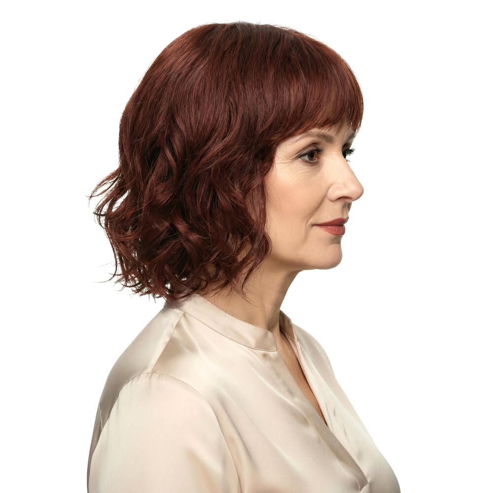 Rote Perücke mit gewelltem Haar und Pony. Seitenansicht einer Frau mit hellem Oberteil.