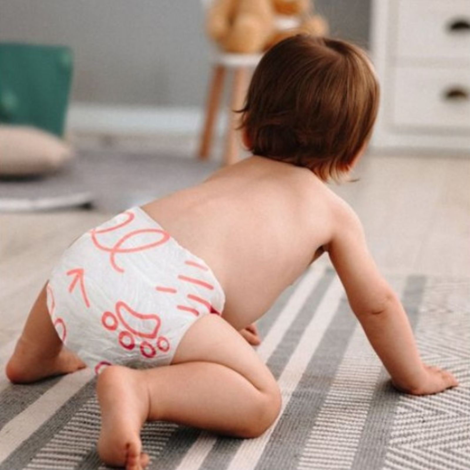Baby krabbelt auf einem Teppich. Windel mit rosa Aufdruck. Marke nicht sichtbar.