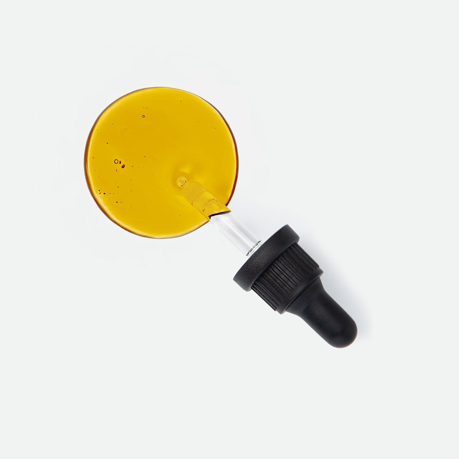 Pipette mit einem Tropfen goldgelbem Öl auf weißem Grund. Nahaufnahme des Öls und der Pipettenspitze.