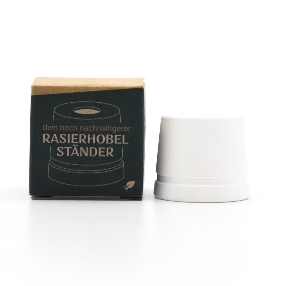 Weißer Rasierhobel-Ständer neben einer Verpackung. Auf der Verpackung steht "RASIERHOBEL STÄNDER".