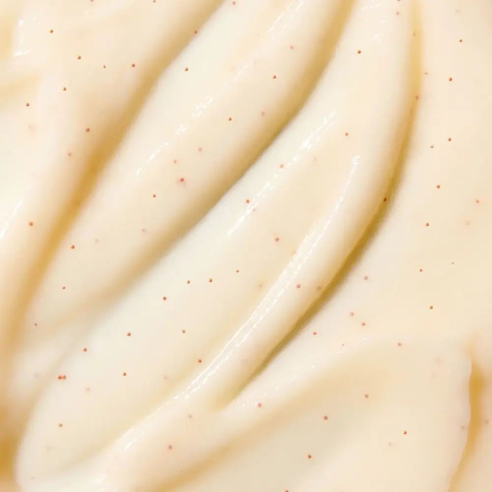 Nahaufnahme einer cremigen Substanz mit kleinen roten Partikeln. Cremefarbene Textur.