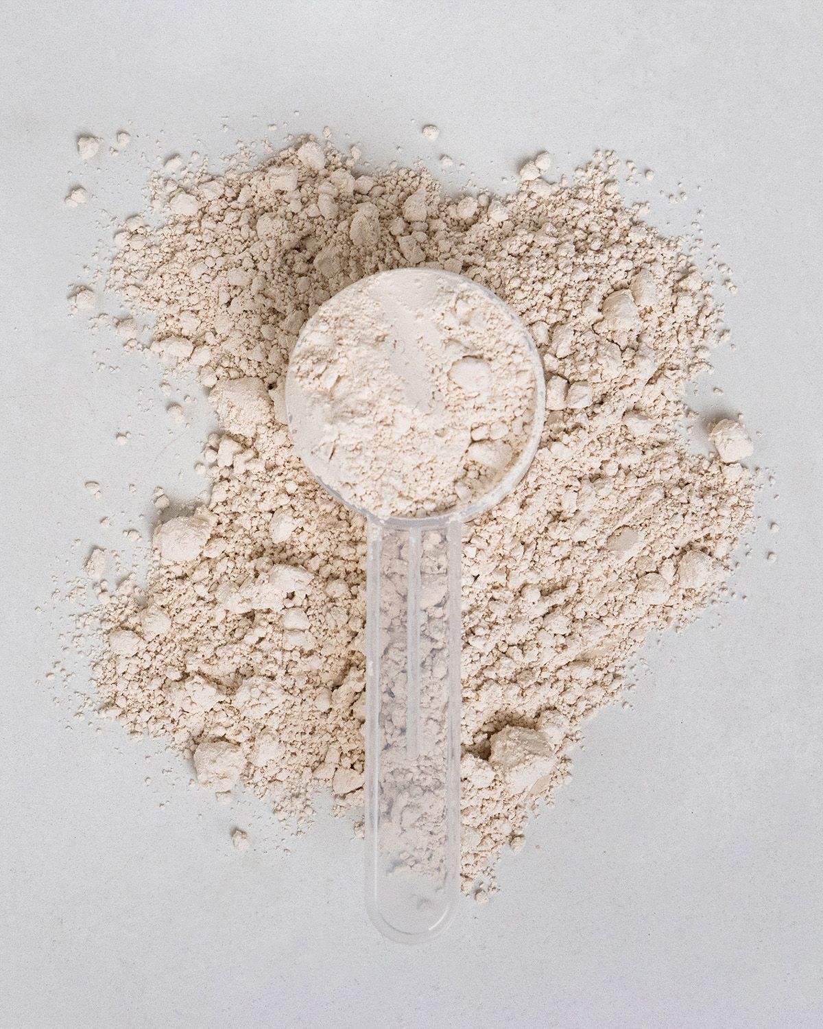 Haufen Reisprotein Pulver und Messlöffel. Helle, beige Farbe. Auf hellem Hintergrund.