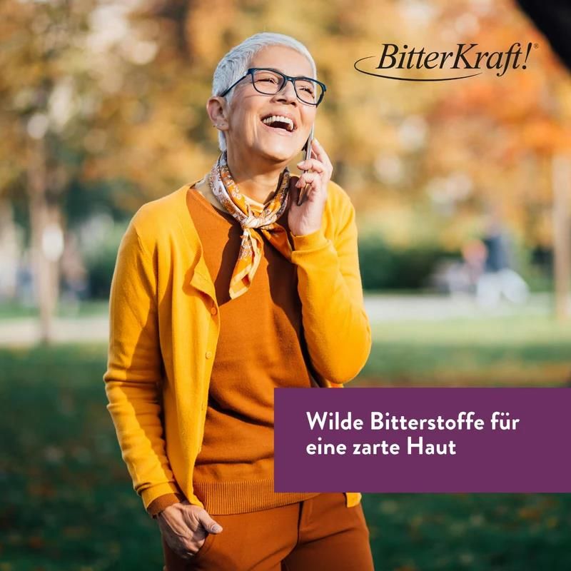 Ältere Frau mit Brille und gelber Jacke telefoniert. Text: Wilde Bitterstoffe für eine zarte Haut. Hintergrund: verschwommener Park.