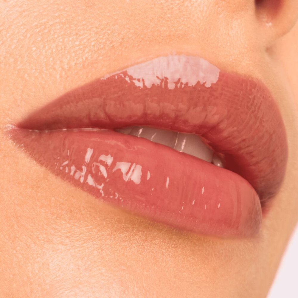 Nahaufnahme von Lippen mit glänzendem Lipgloss. Rosa Farbton. Ober- und Unterlippe sichtbar. Glanz reflektiert Licht.