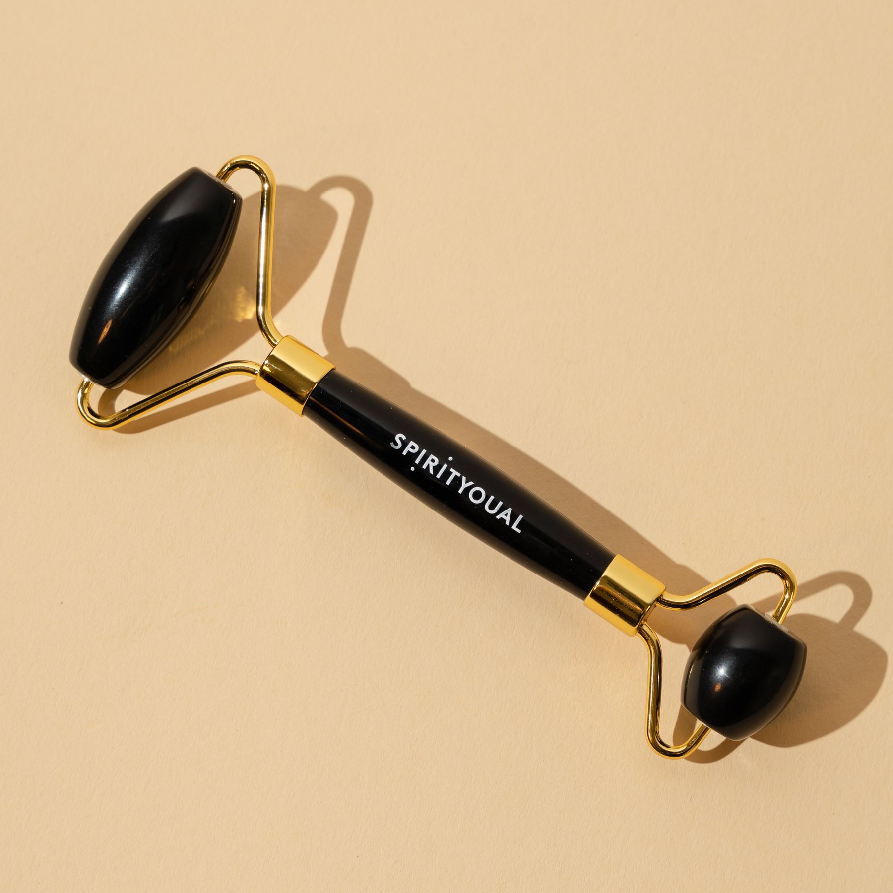 Schwarzer Beauty-Roller mit goldenen Details. Schriftzug SPIRITYOUAL. Auf beigem Untergrund. Zwei Rollen an den Enden, eine in der Mitte.