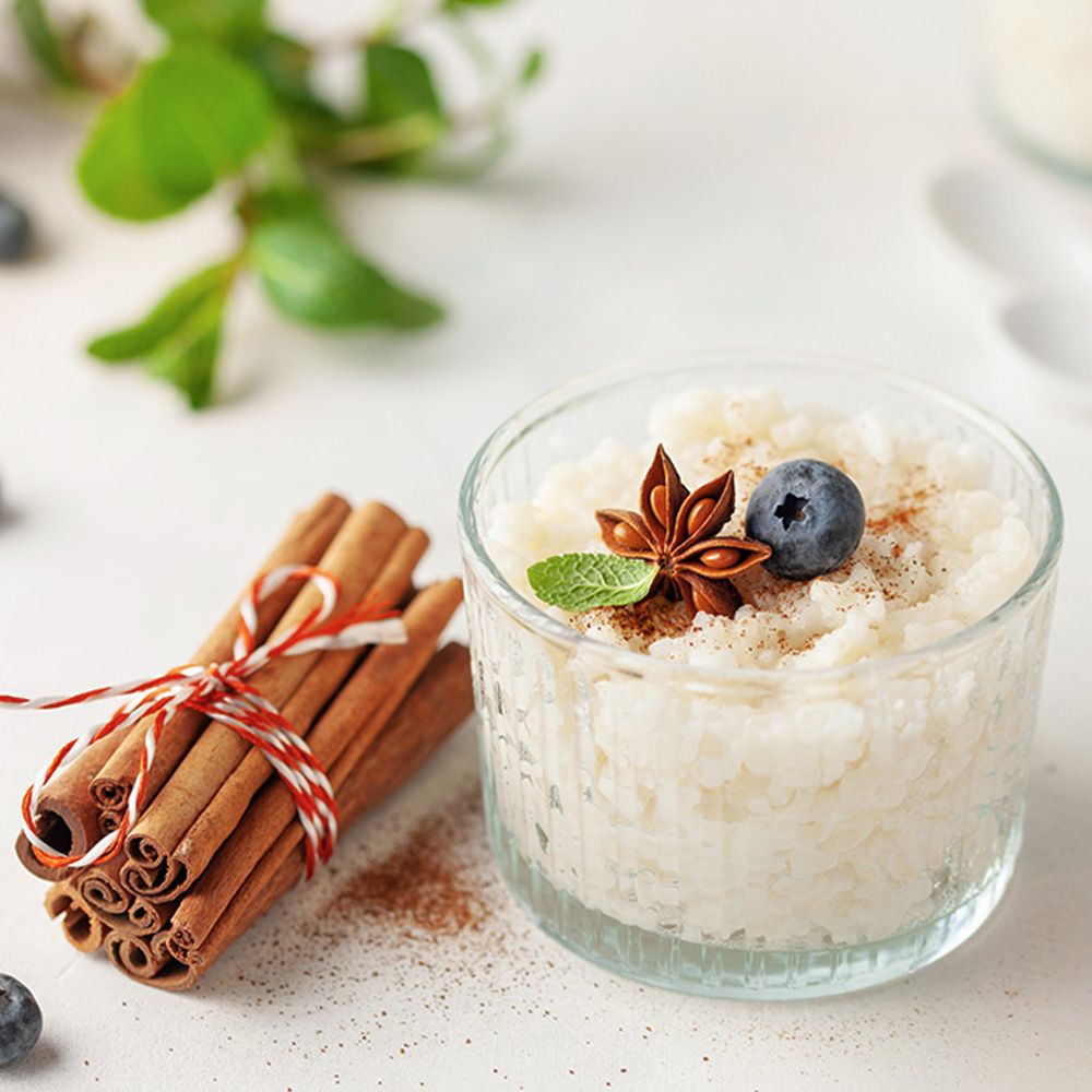 Glas mit Reis-Pudding, dekoriert mit Blaubeere, Sternanis und Minze. Zimtstangen gebündelt mit Schnur.