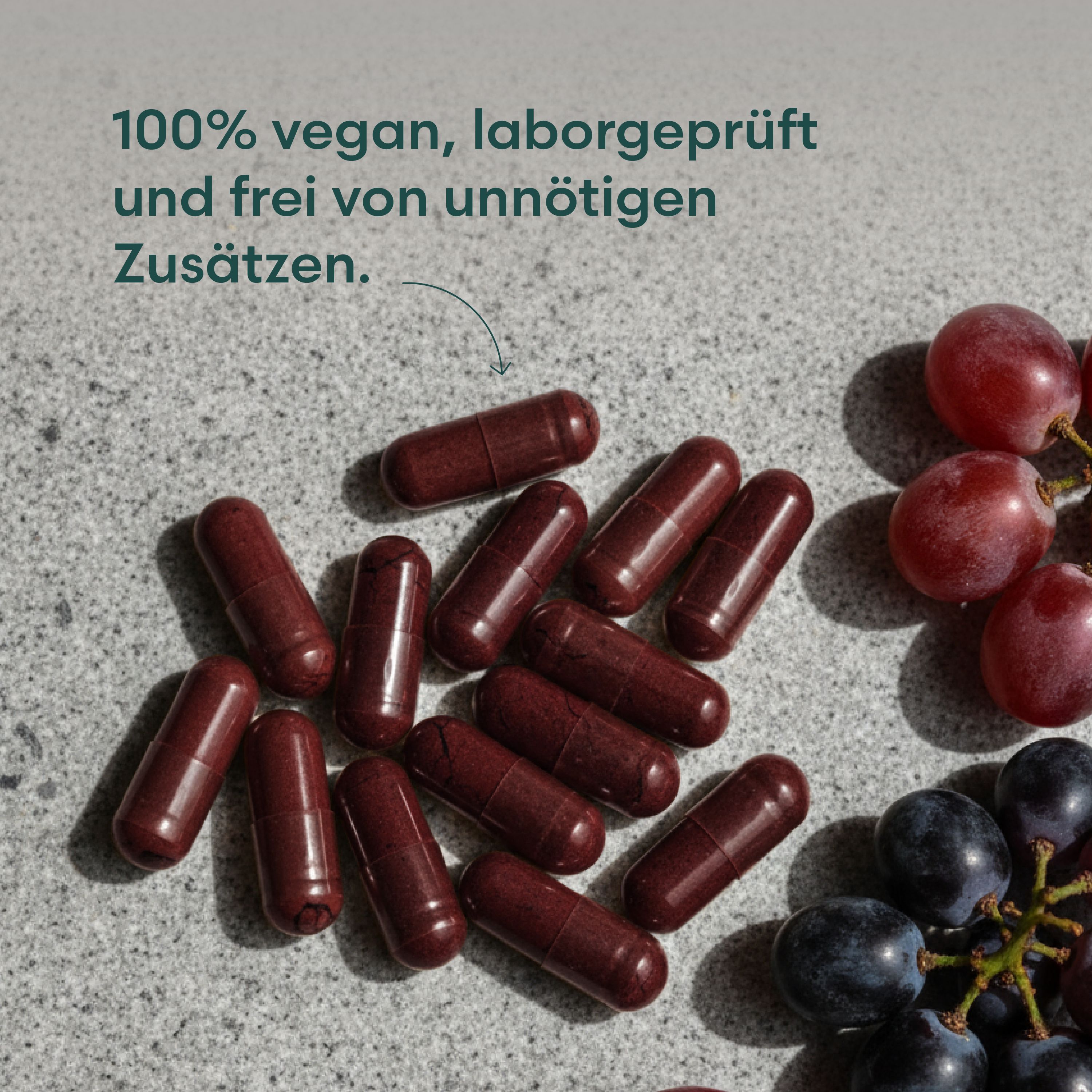 Braune Kapseln und rote Trauben auf grauem Untergrund. Keine Verpackung sichtbar.