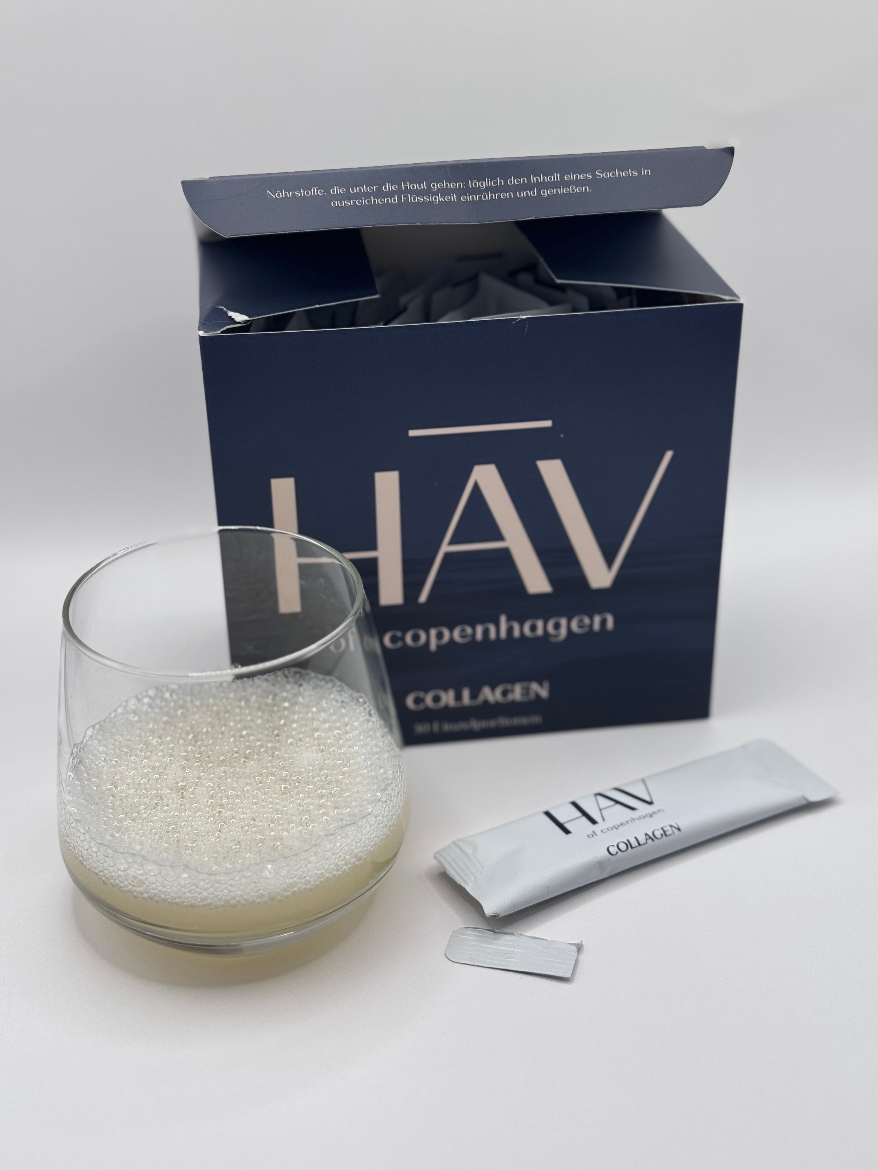 Glas mit Flüssigkeit und Collagen-Stick neben einer geöffneten HAV-Schachtel.