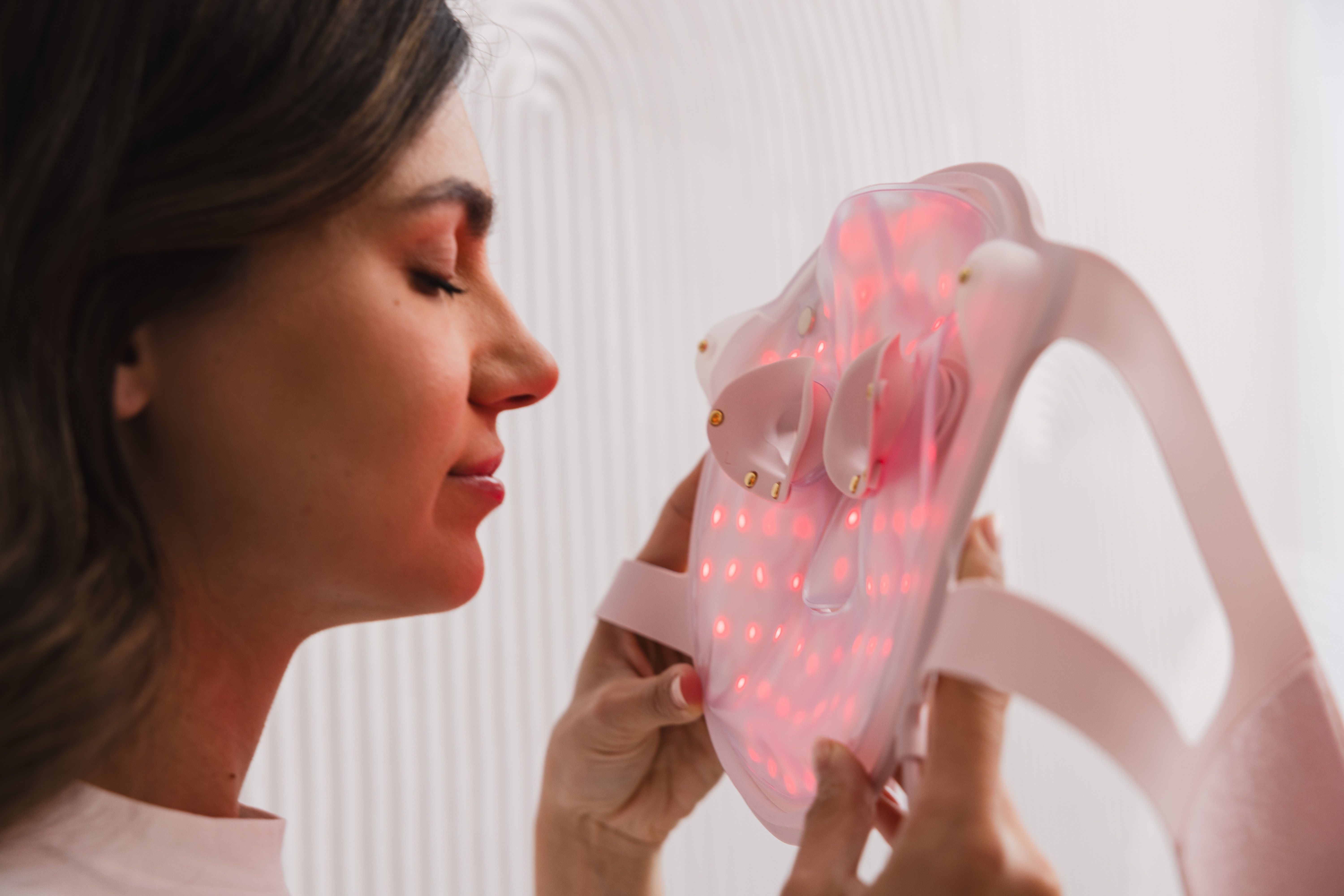 Person hält eine rosa LED-Gesichtsmaske. Die Maske leuchtet rot. Nahaufnahme der Augenpartie.