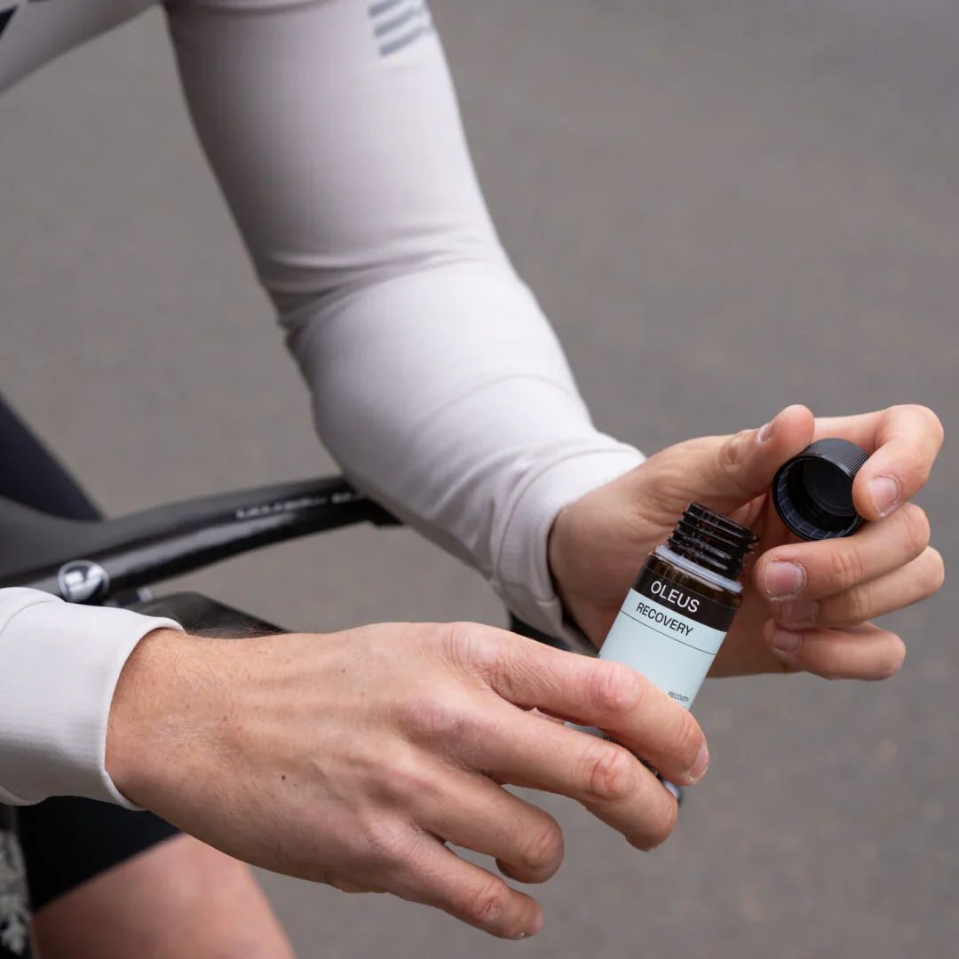 Person öffnet Flasche. OLEUS RECOVERY-Etikett sichtbar. Schwarzer Deckel.