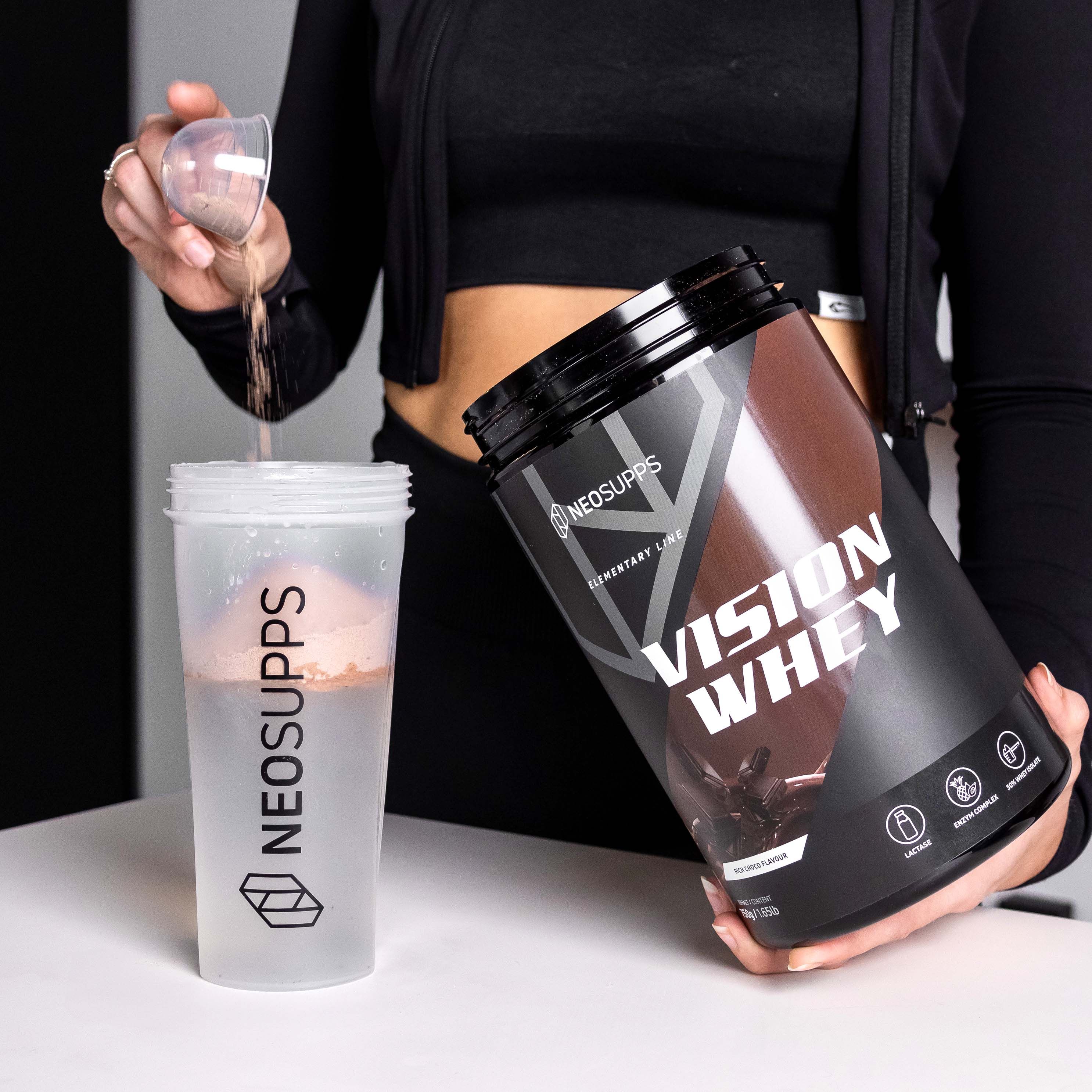 Person gießt Pulver in einen Shaker. Daneben steht eine Dose Vision Whey. Aufschrift: Vision Whey. Shaker mit Flüssigkeit.