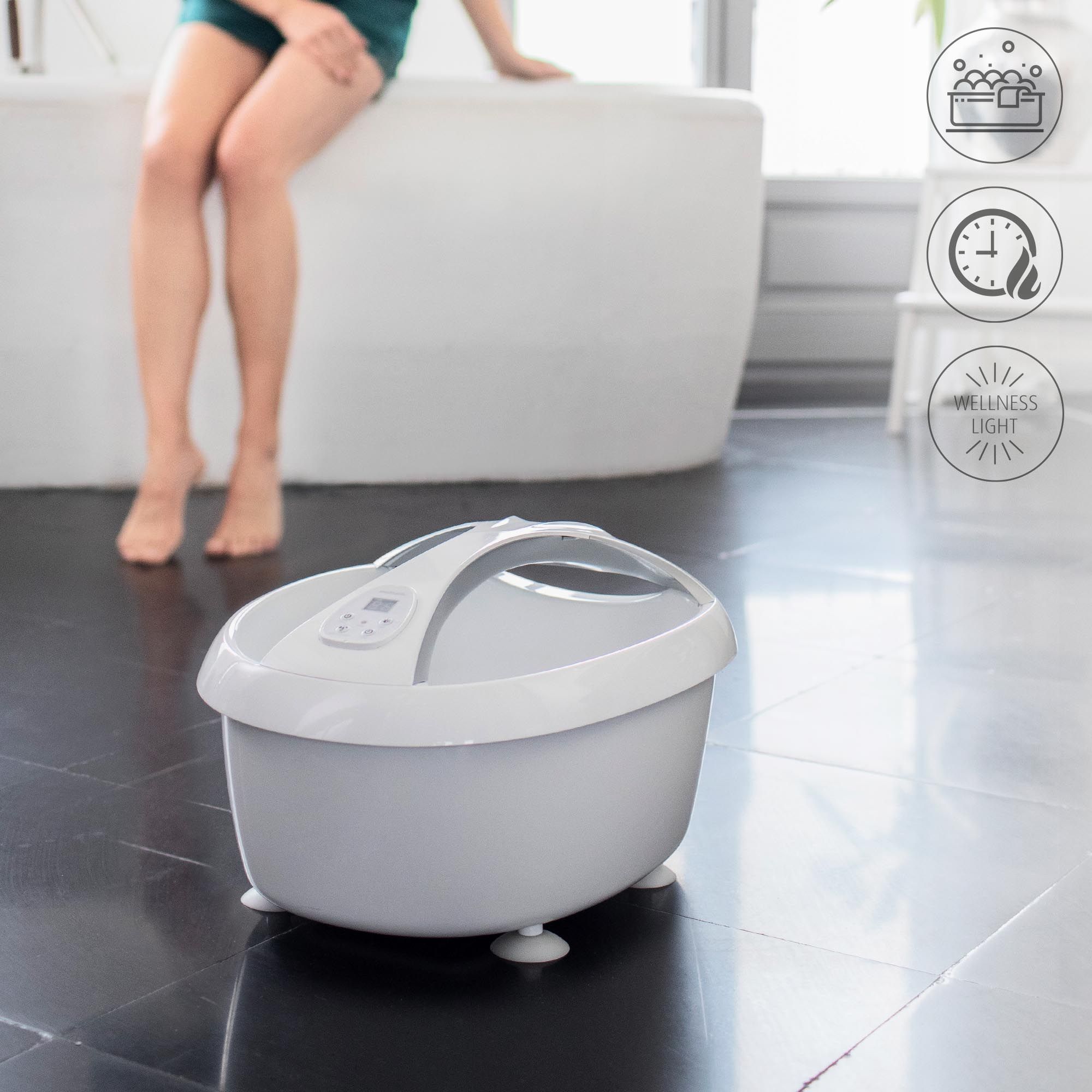 Graues Fußbad mit Griff und Füßen. Wellness-Symbole im Hintergrund.