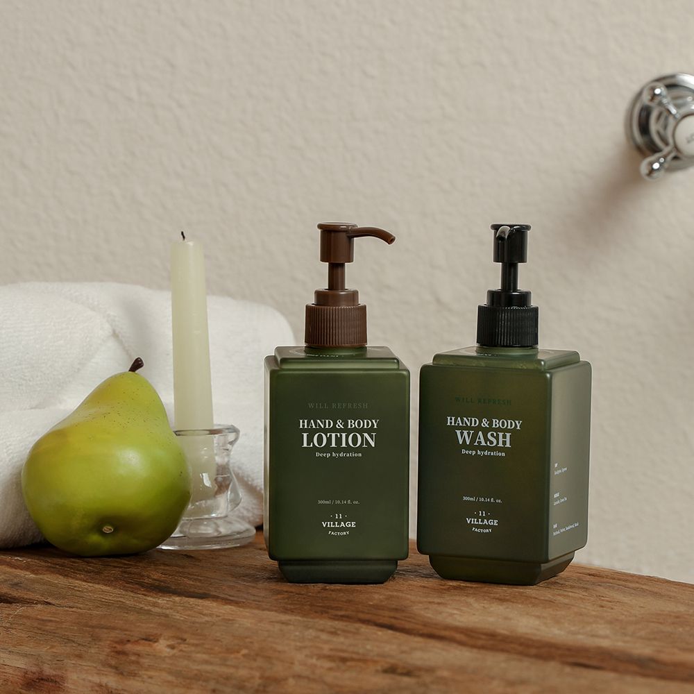 Zwei grüne Flaschen mit Pumpköpfen. Text: Hand & Body Lotion, Hand & Body Wash, 11 Village Factory. Kerze, Birne, Handtuch.