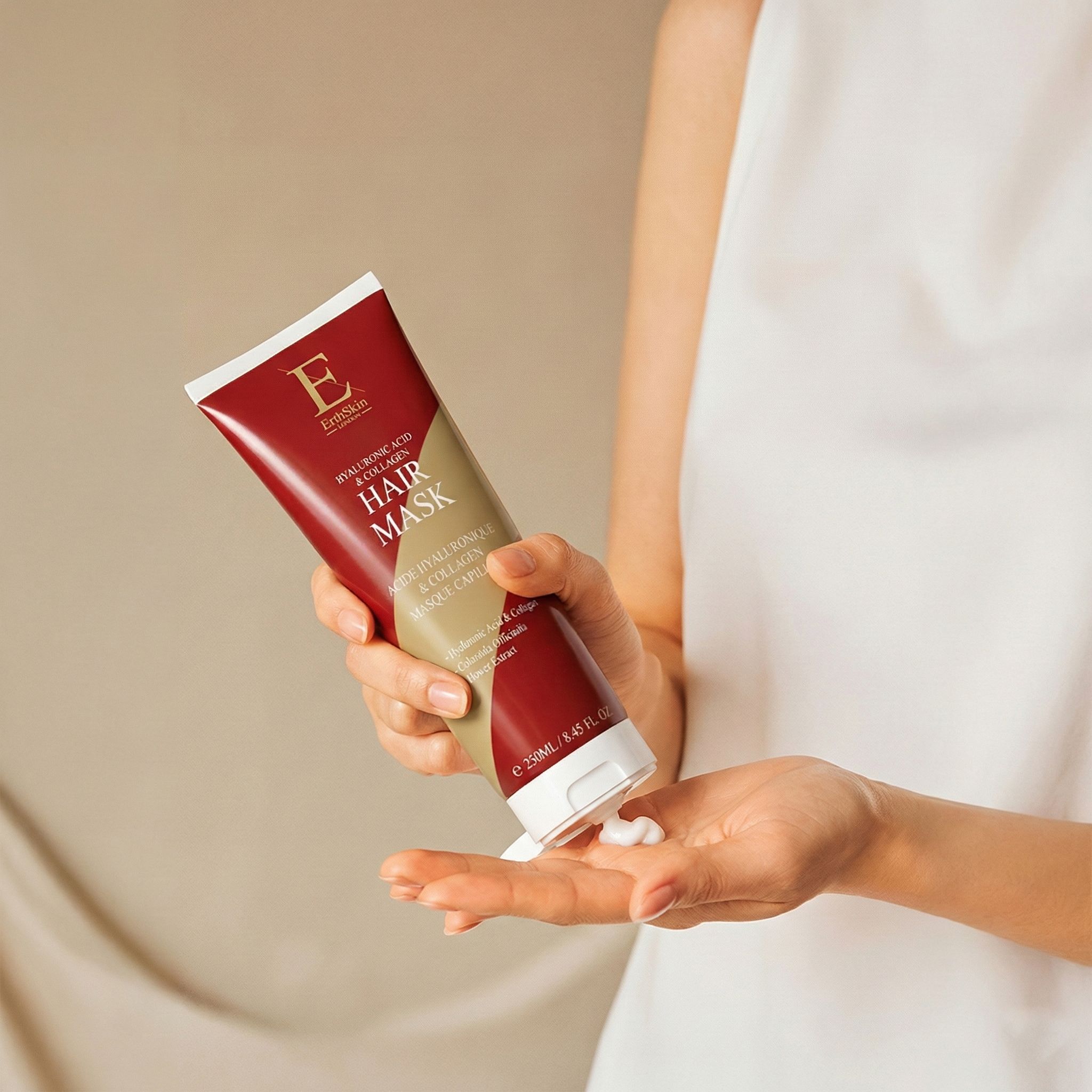 Eine Hand hält eine rote Tube mit Hyaluronsäure & Kollagen Haarmaske. Etwas Creme wird herausgedrückt.