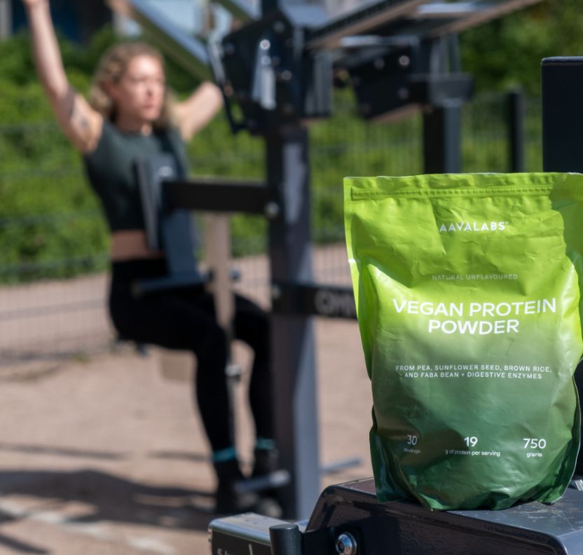 Aavalaabs veganes Proteinpulver neben Trainingsgerät im Freien, Frau trainiert.