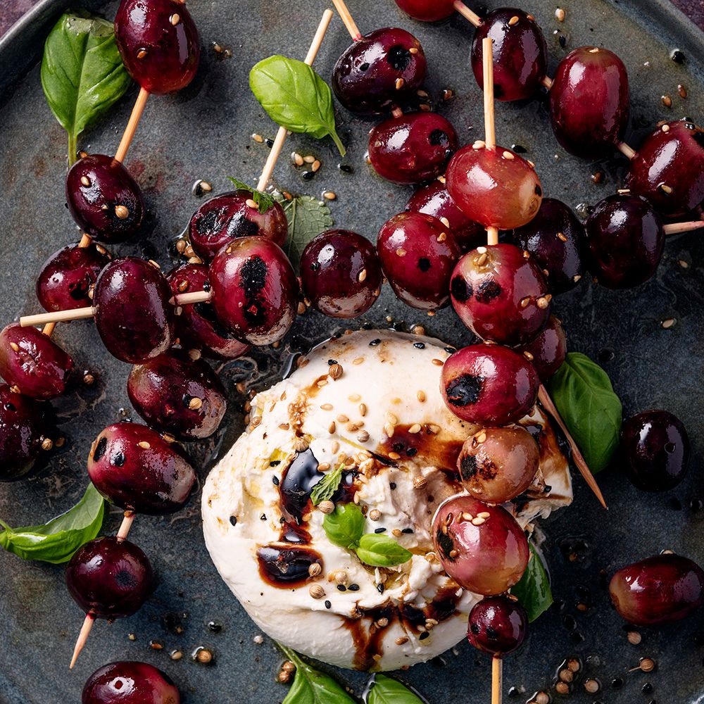 Teller mit Trauben-Spießen, Burrata und Basilikum. Trauben auf Holzspießen, Burrata mit Balsamico-Glasur.