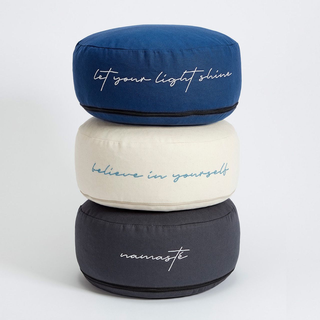 Drei Meditationskissen gestapelt: blau, cremefarben, grau. Mit Schriftzügen: "let your light shine", "believe in yourself", "namasté".