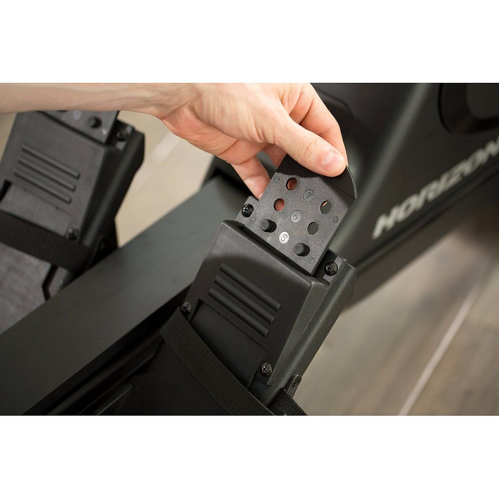 Nahaufnahme einer Person, die ein schwarzes Teil an einem Rudergerät befestigt. Schrauben sichtbar.